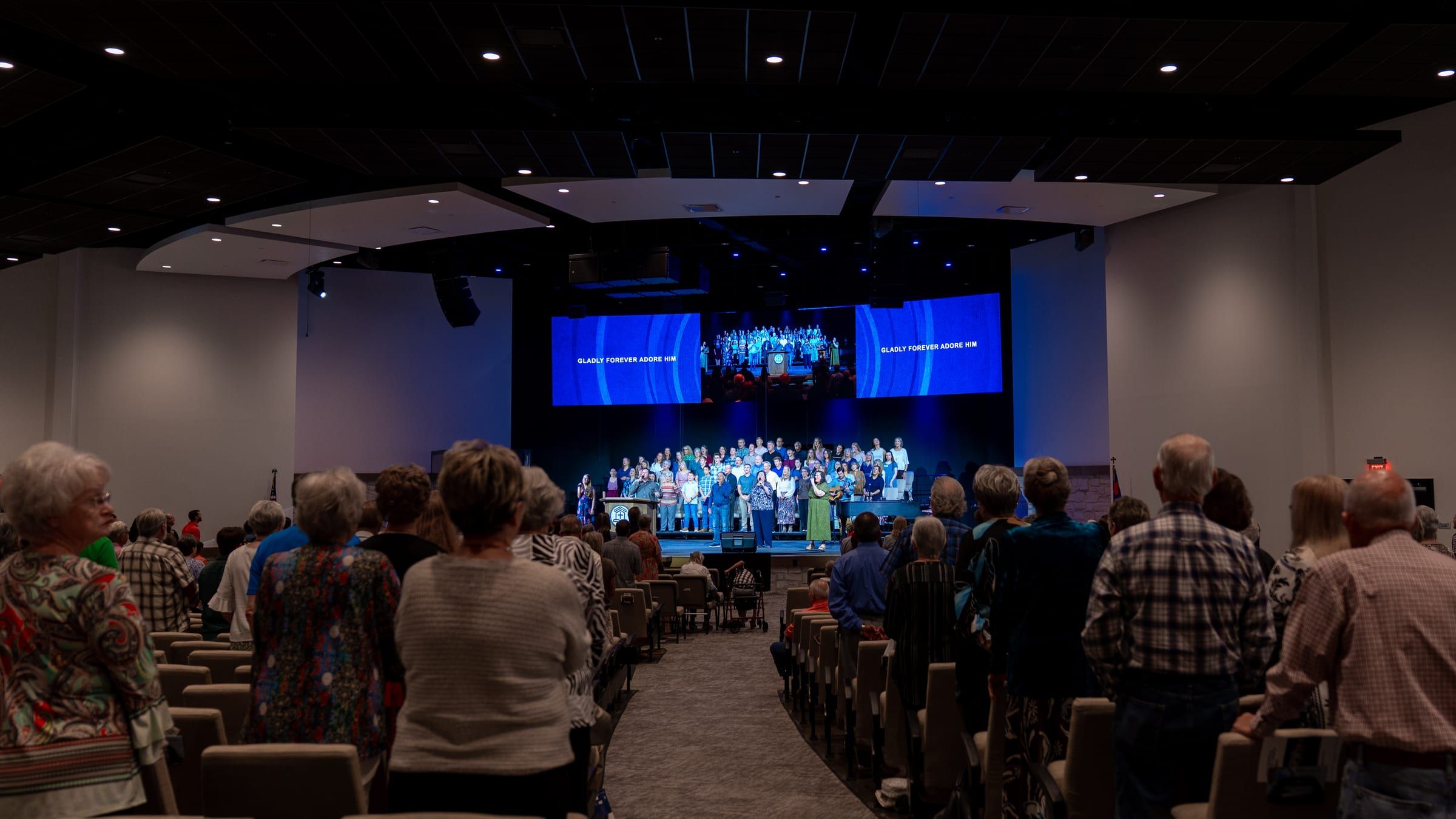 The congregation standing in worship facing the choir and stage during a Sunday morning service.