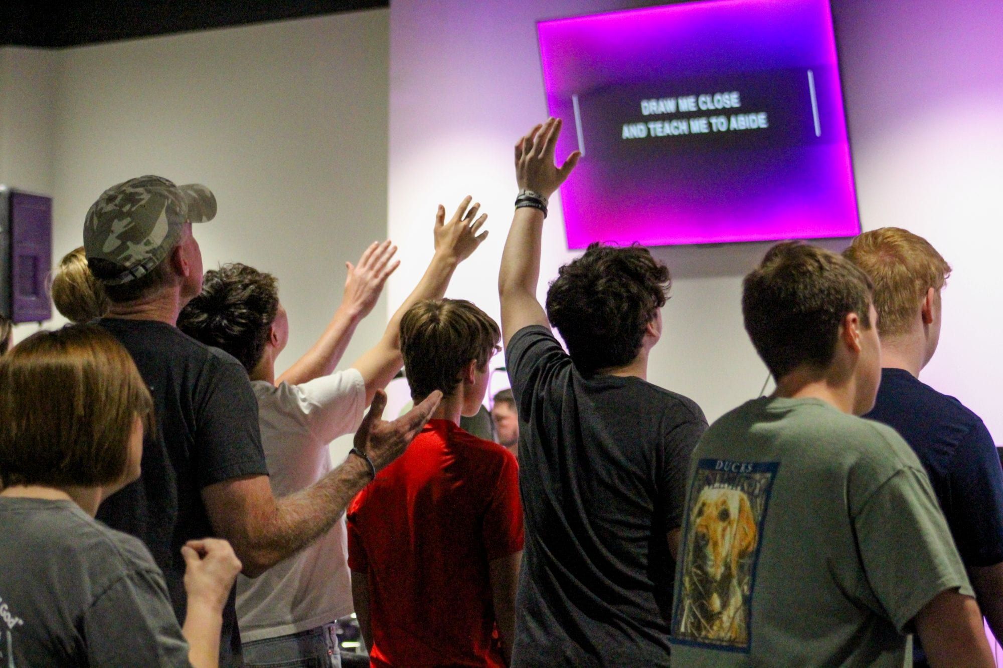 Students worshipping with raised hands in the student ministry room.