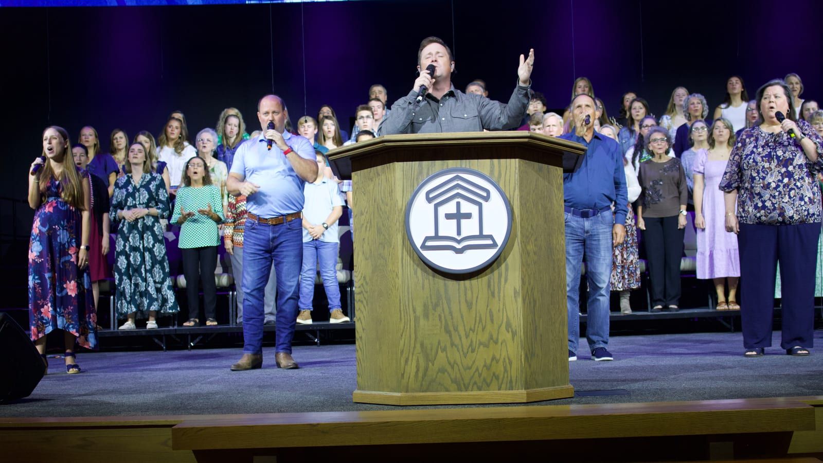 The worship leader singing with a hand raised as the praise team and choir sing behind him.